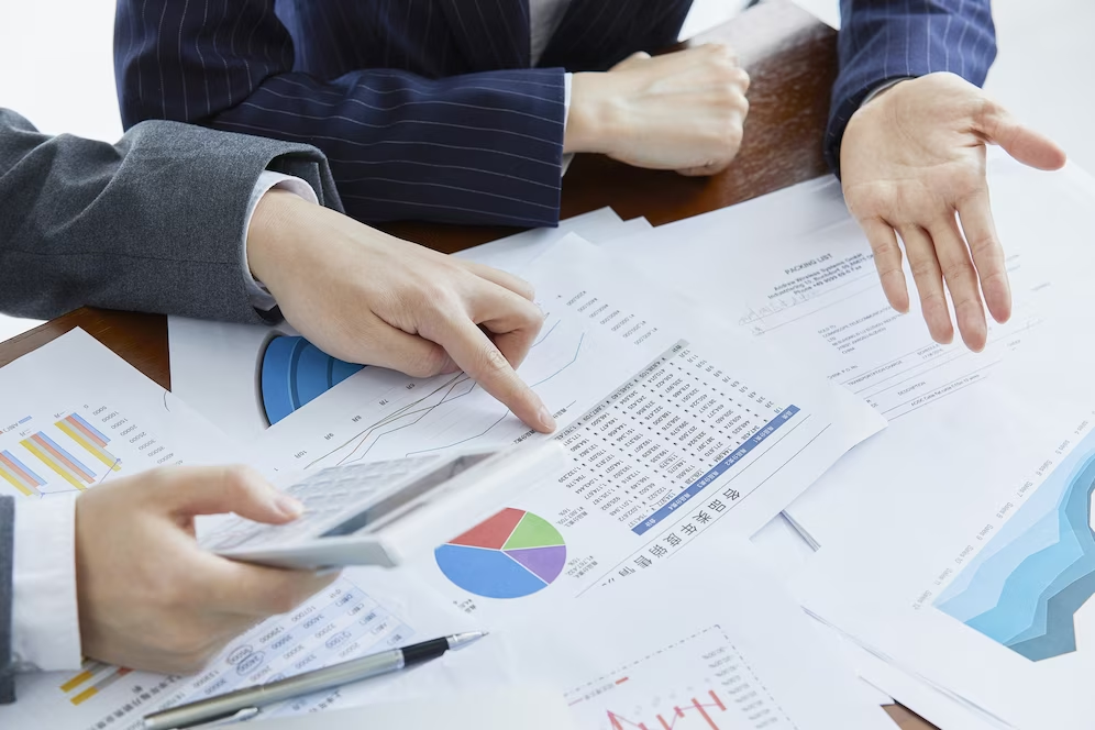 Two people discussing financial projections with documents, graphs, and pie charts on the table.