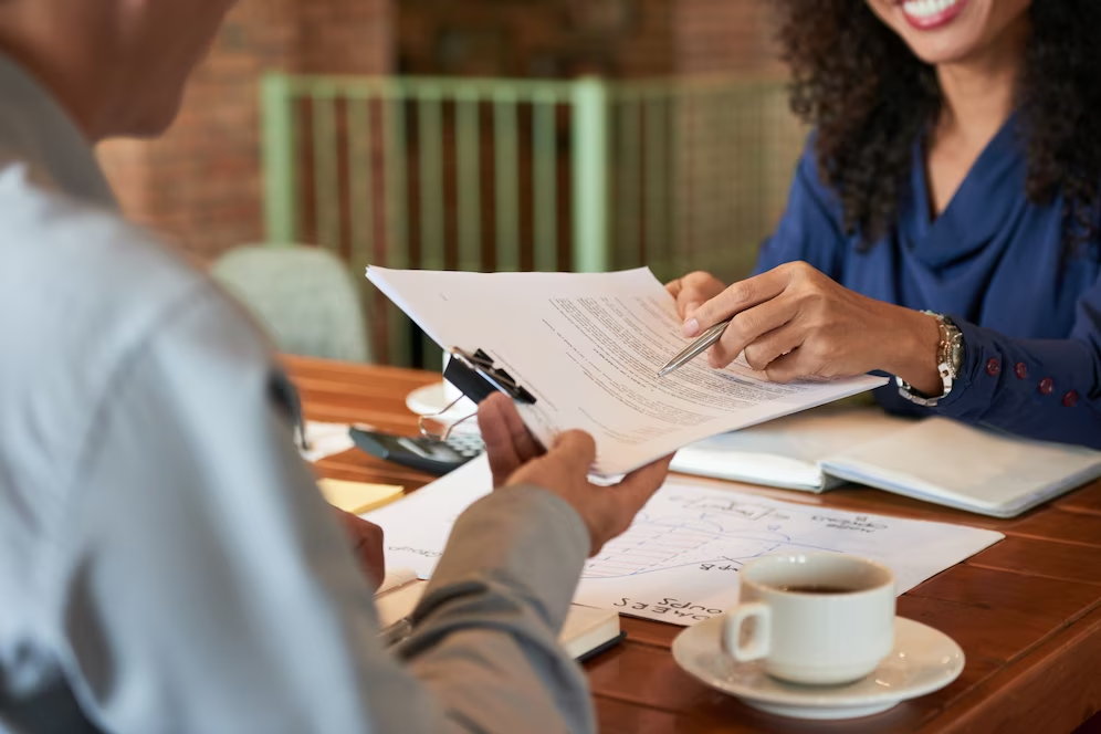 A smiling woman holding documents, pointing at something on the document while engaging with client