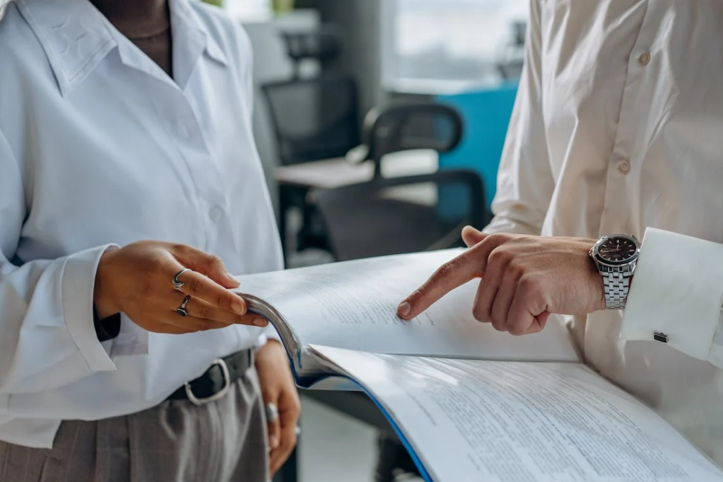 two people are standing in the office and talking, holding a book