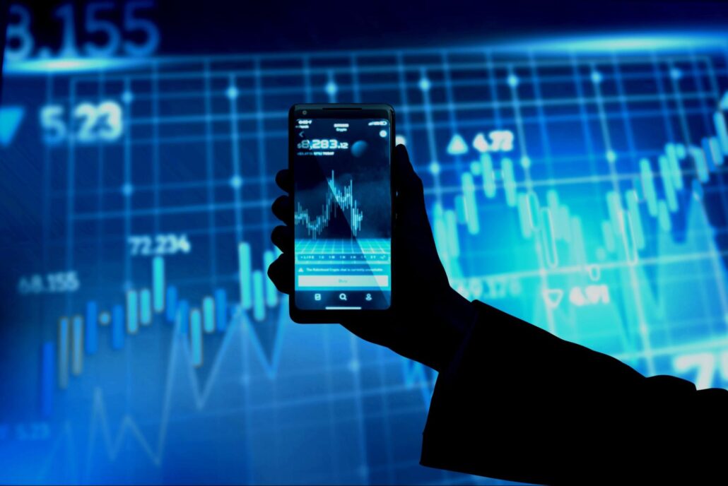 a hand holding a cell phone against the dark-blue background with graphs and numbers