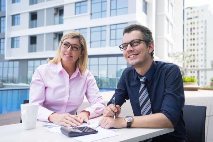 a couple of smiling and ambitious accountants sitting at table with papers and a calculator