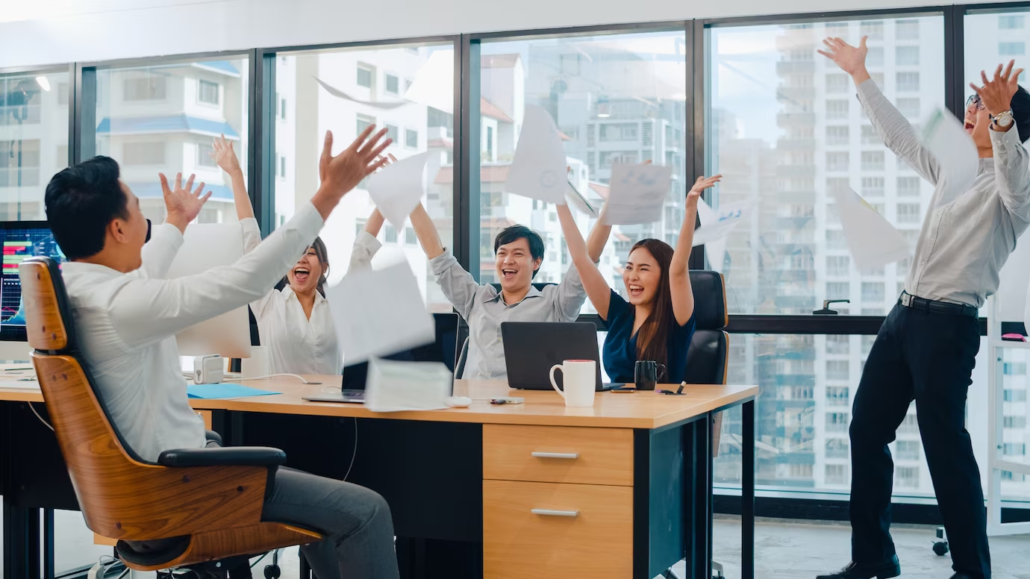 Group of people inside an office raising their hands in celebration.