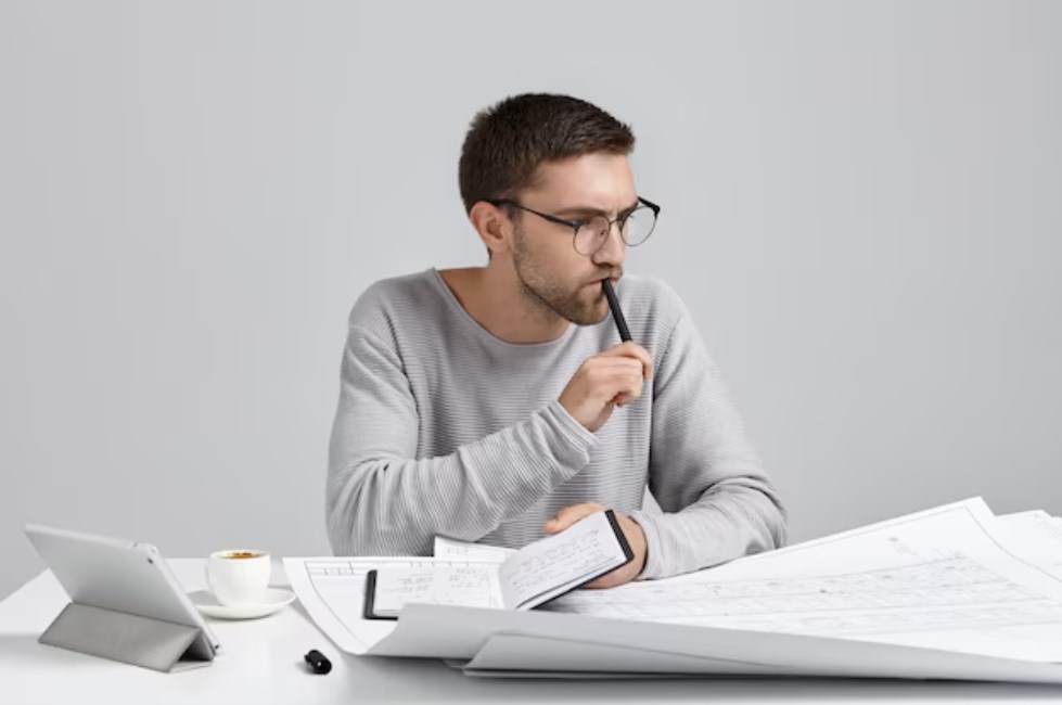 a serious pensive male engineer in glasses holding a pen and a notebook in his hands