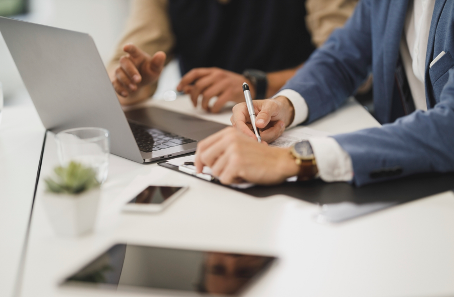 People's hands on the table, a laptop, a tablet and a glass of drink are in front of them