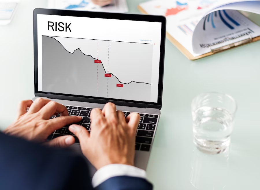 Photo of a hand typing on a laptop, with a line graph displayed on the monitor and the text 'risk' visible