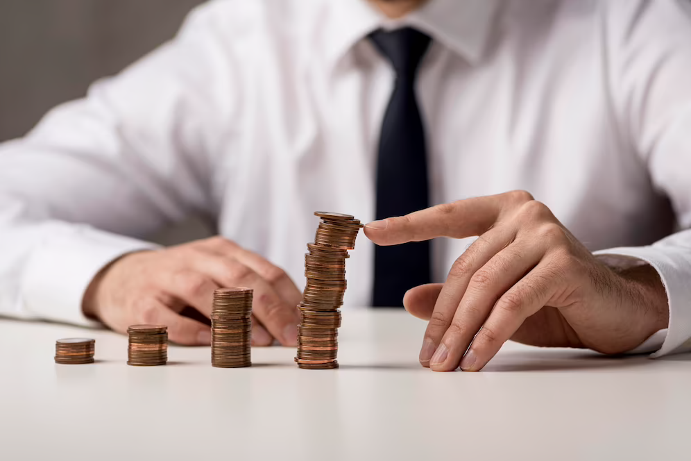 Coins stacked on a table with a hand saving the tallest tower from falling