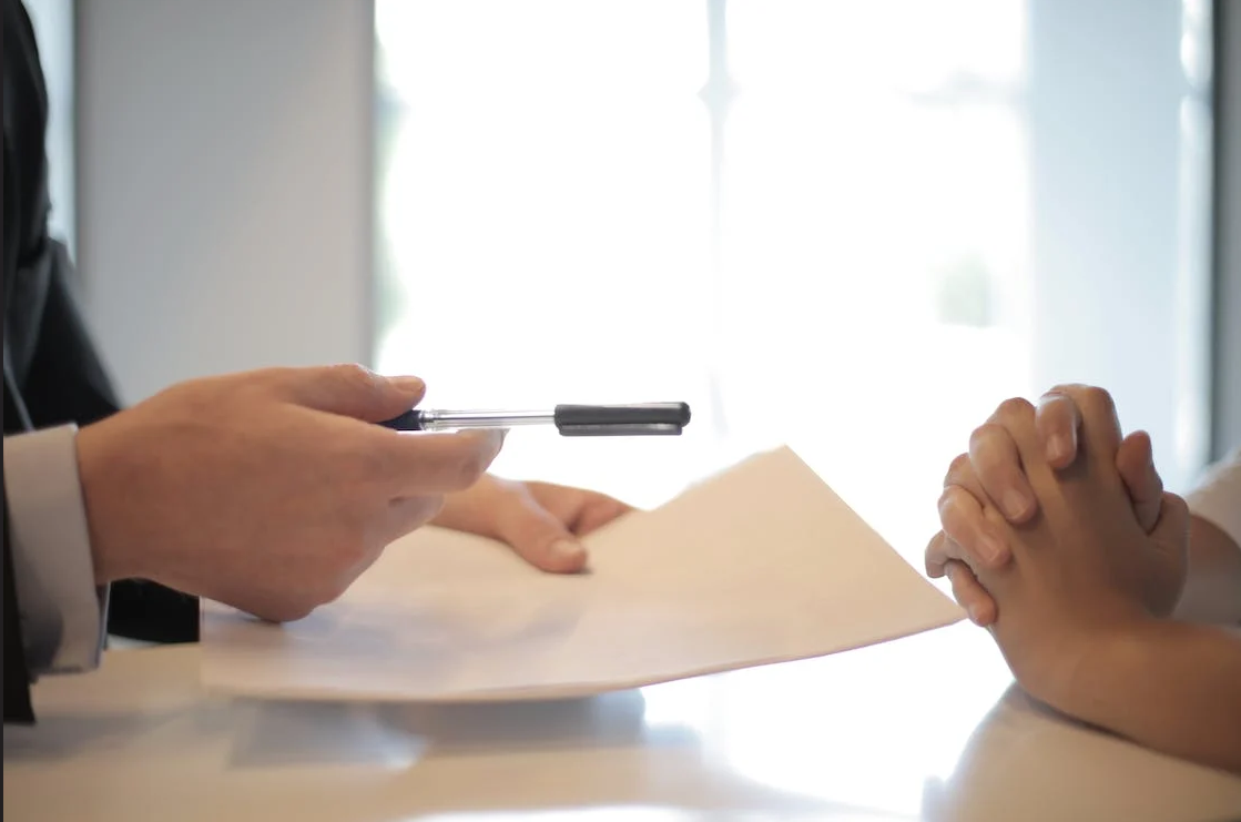 a dialogue at the table between two people, one handing the other a piece of paper and a pen