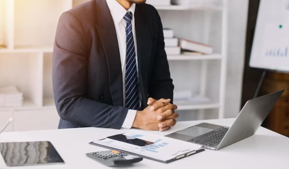 an investment banker with his hands crossed at the office table with a laptop and a calculator